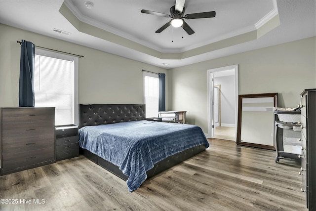 bedroom featuring visible vents, ornamental molding, a raised ceiling, and wood finished floors