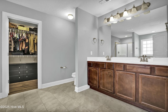 bathroom featuring tile patterned floors, toilet, a stall shower, double vanity, and baseboards