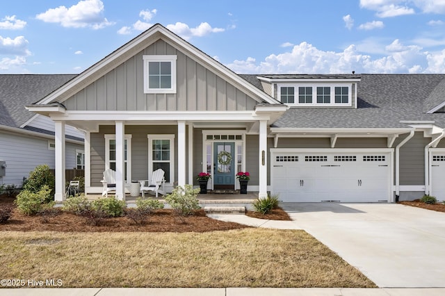 view of front of property featuring driveway, roof with shingles, an attached garage, covered porch, and board and batten siding