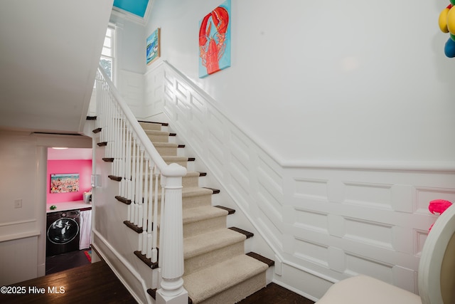 staircase featuring a wainscoted wall, washer / dryer, wood finished floors, and a decorative wall