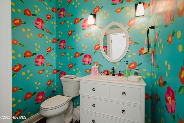 half bathroom featuring baseboards, toilet, vanity, and wallpapered walls