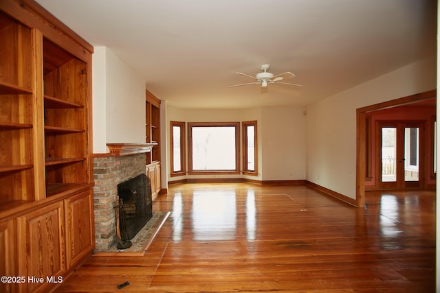 unfurnished living room featuring built in features, a ceiling fan, baseboards, a fireplace, and light wood-type flooring