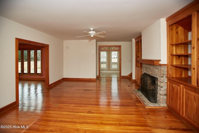 unfurnished living room with a ceiling fan, a brick fireplace, baseboards, and light wood-type flooring