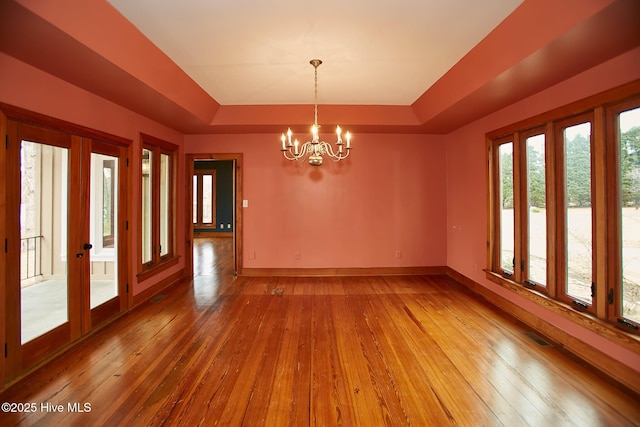 interior space with baseboards, a tray ceiling, french doors, light wood-style floors, and a notable chandelier