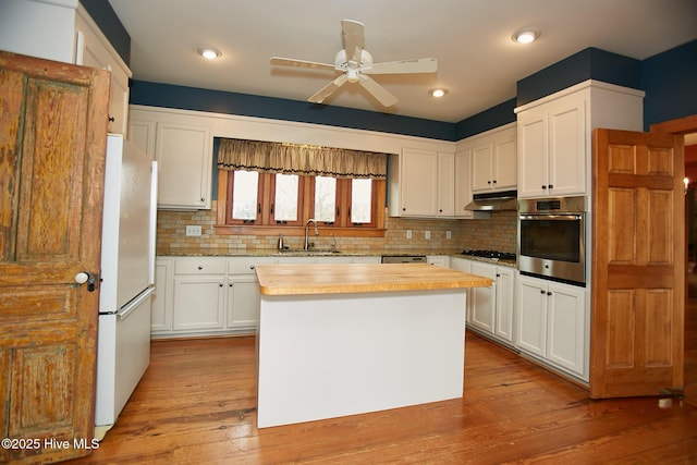 kitchen featuring gas cooktop, freestanding refrigerator, a sink, oven, and under cabinet range hood