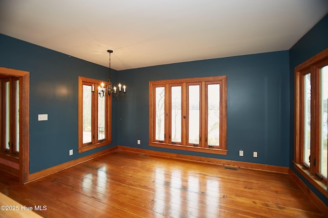 empty room with baseboards, wood-type flooring, visible vents, and a chandelier