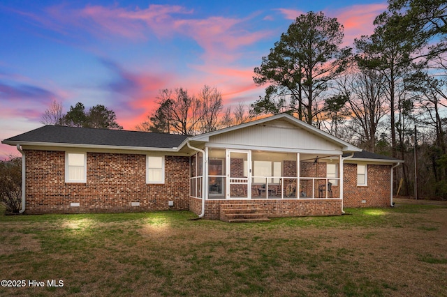 back of house at dusk featuring crawl space, brick siding, a yard, and a sunroom