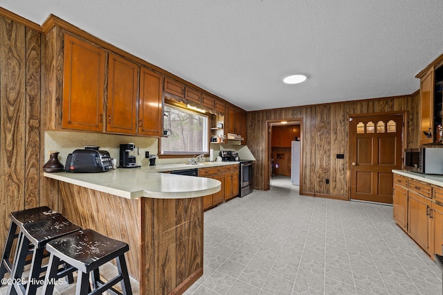 kitchen featuring wooden walls, light countertops, appliances with stainless steel finishes, a peninsula, and brown cabinetry