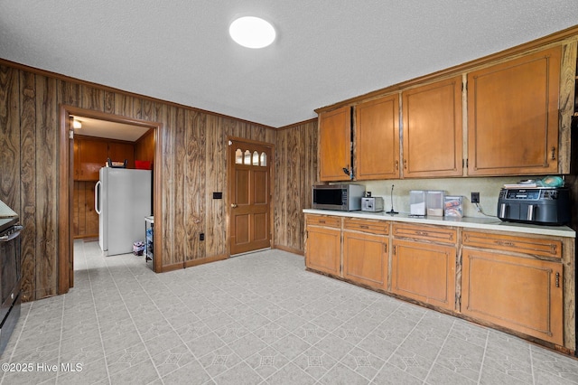 kitchen with brown cabinetry, stainless steel microwave, light countertops, and freestanding refrigerator