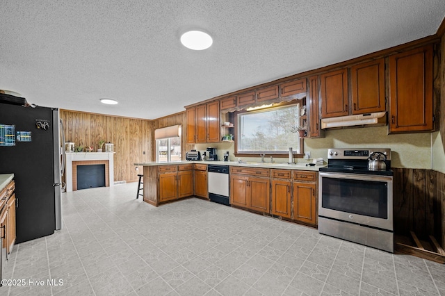 kitchen with under cabinet range hood, wooden walls, appliances with stainless steel finishes, a peninsula, and light countertops