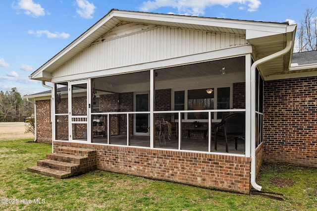 back of house featuring brick siding, a yard, and a sunroom