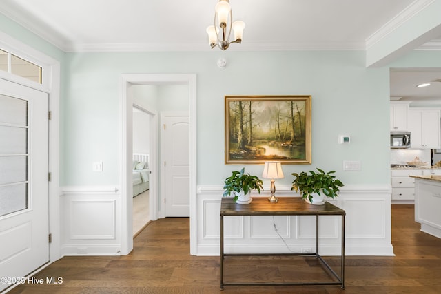 hall featuring a notable chandelier, dark wood-style floors, wainscoting, and ornamental molding