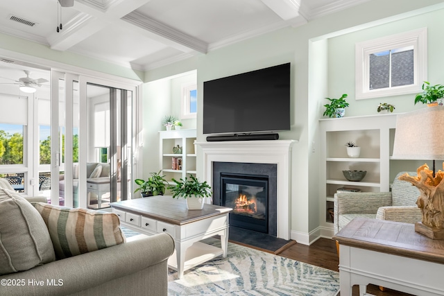 living area with beam ceiling, a glass covered fireplace, ceiling fan, and wood finished floors