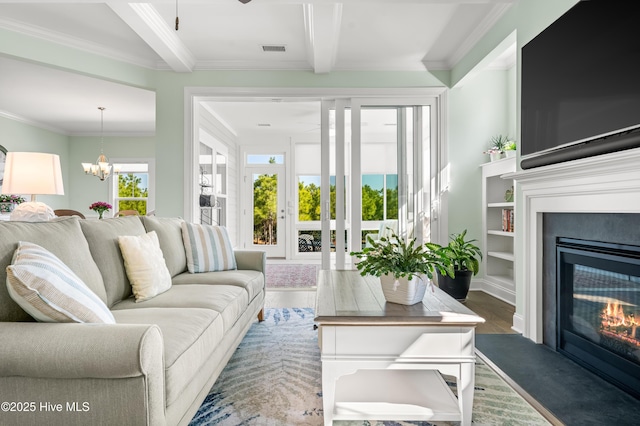 living room featuring wood finished floors, visible vents, a glass covered fireplace, crown molding, and a notable chandelier