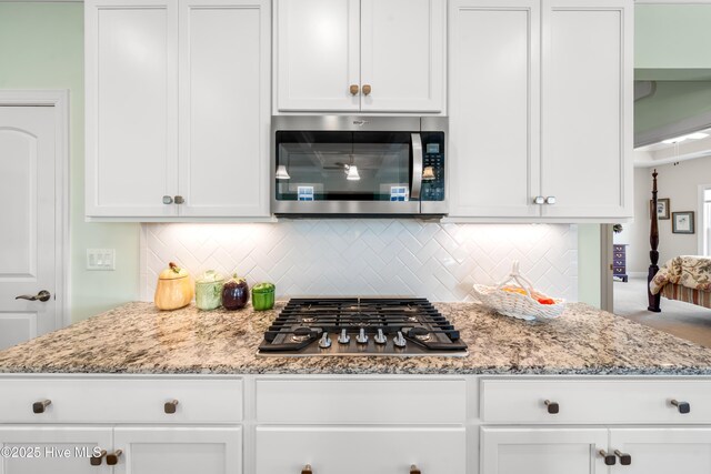 kitchen with decorative backsplash, white cabinets, stainless steel appliances, and light stone countertops