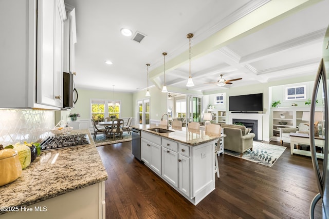 kitchen with light stone countertops, dark wood finished floors, beam ceiling, stainless steel appliances, and a sink