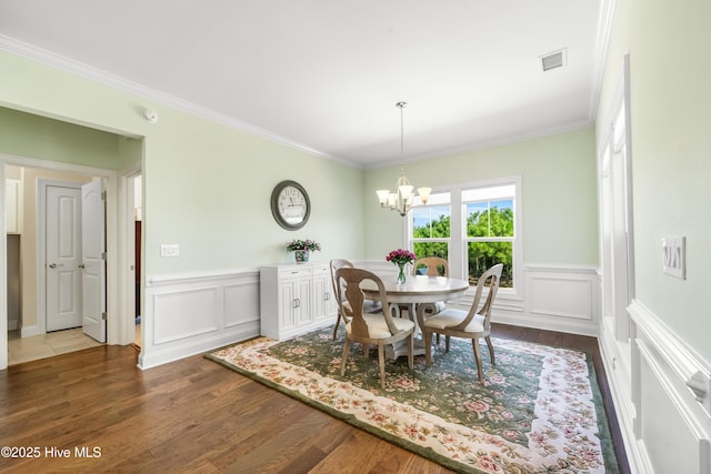 dining area with visible vents, dark wood-type flooring, an inviting chandelier, and ornamental molding