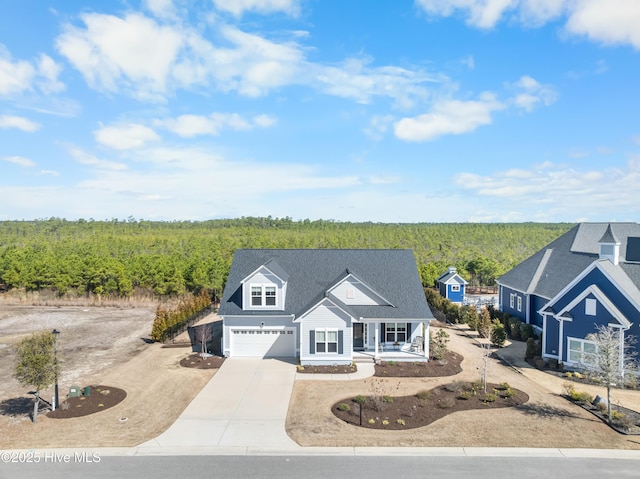 view of front of house with a wooded view, driveway, roof with shingles, covered porch, and a garage