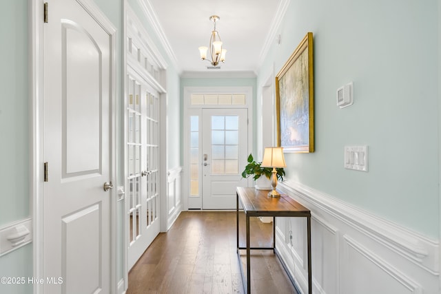 entrance foyer with a wainscoted wall, dark wood finished floors, an inviting chandelier, crown molding, and a decorative wall