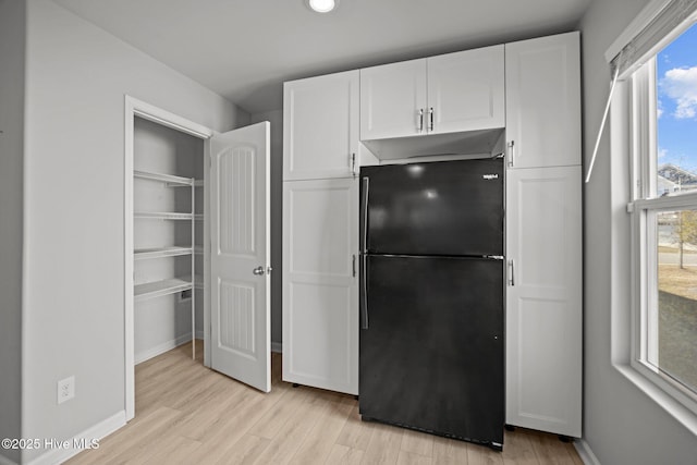 kitchen with white cabinetry, light wood-style floors, baseboards, and freestanding refrigerator