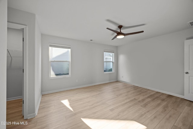 unfurnished bedroom with visible vents, a walk in closet, baseboards, light wood-style floors, and a closet