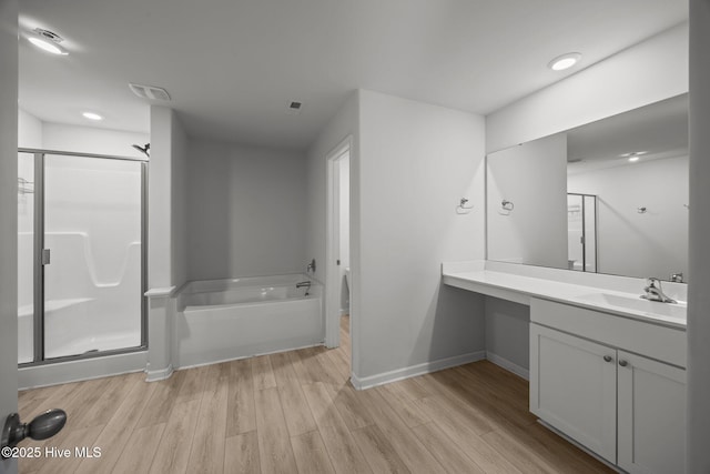 full bath featuring a stall shower, wood finished floors, baseboards, a bath, and vanity