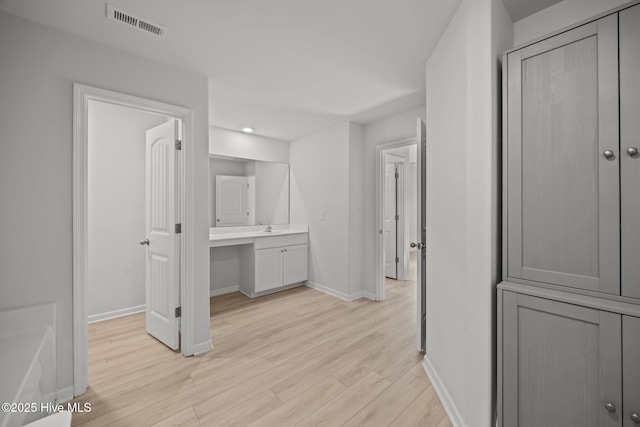 hallway with visible vents, baseboards, light wood finished floors, and a sink