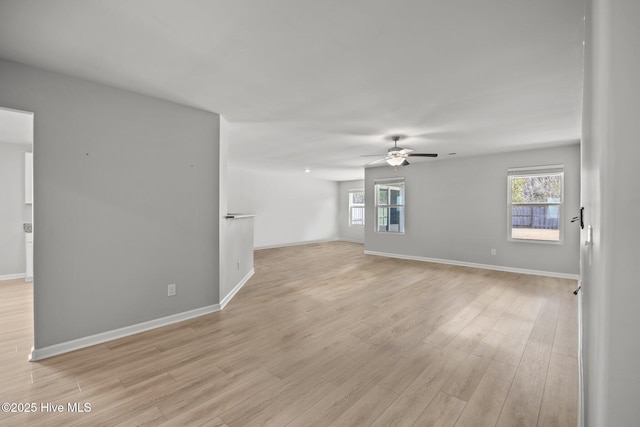 empty room with a wealth of natural light, baseboards, light wood-style floors, and a ceiling fan