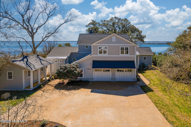 view of front of home with driveway, an attached garage, a shingled roof, a water view, and board and batten siding