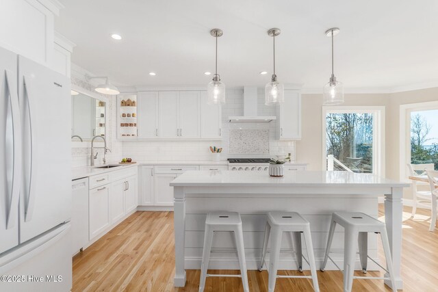 kitchen featuring light countertops, a kitchen breakfast bar, white appliances, wall chimney exhaust hood, and a sink