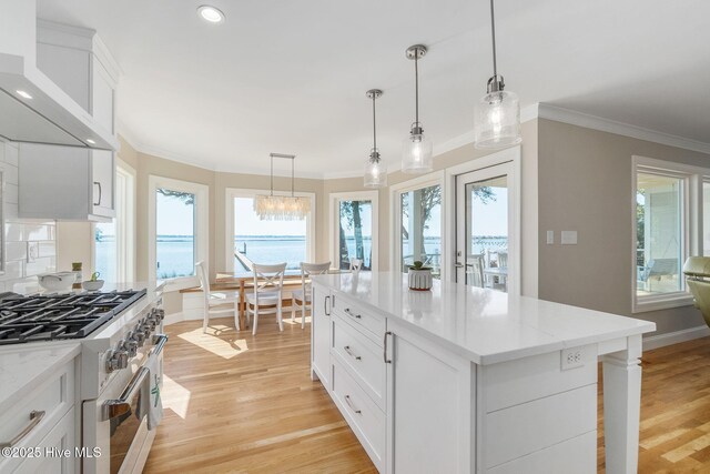 kitchen with light wood-style floors, crown molding, high end range, and wall chimney range hood