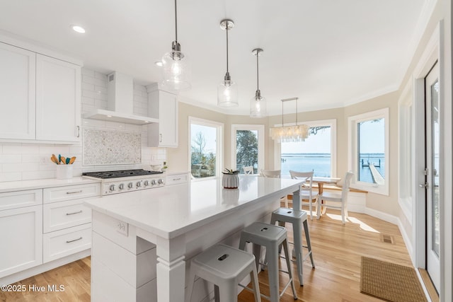 kitchen with white gas cooktop, light wood-style flooring, ornamental molding, wall chimney exhaust hood, and backsplash