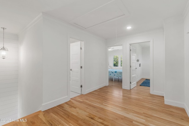 unfurnished room with attic access, crown molding, light wood-type flooring, and baseboards