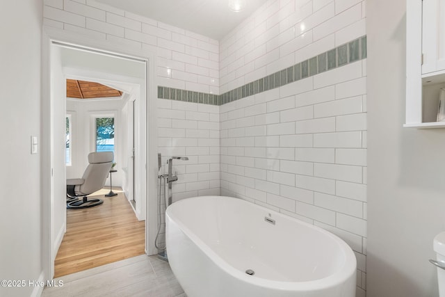 full bath with tile walls, a freestanding tub, and wood finished floors