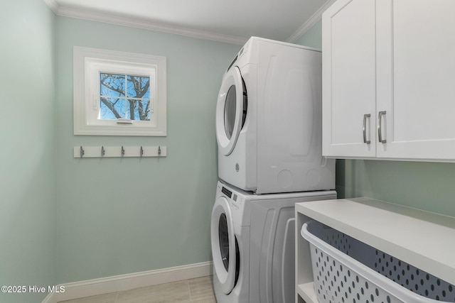 washroom featuring cabinet space, stacked washer and clothes dryer, baseboards, and ornamental molding