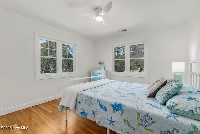 bedroom with visible vents, wood finished floors, baseboards, and ornamental molding