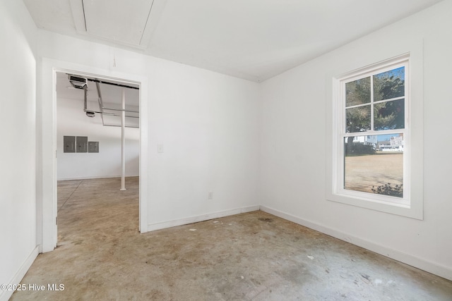 spare room featuring baseboards, attic access, and unfinished concrete floors