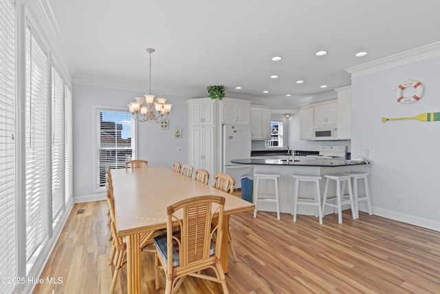 dining room with light wood-type flooring, ornamental molding, recessed lighting, an inviting chandelier, and baseboards