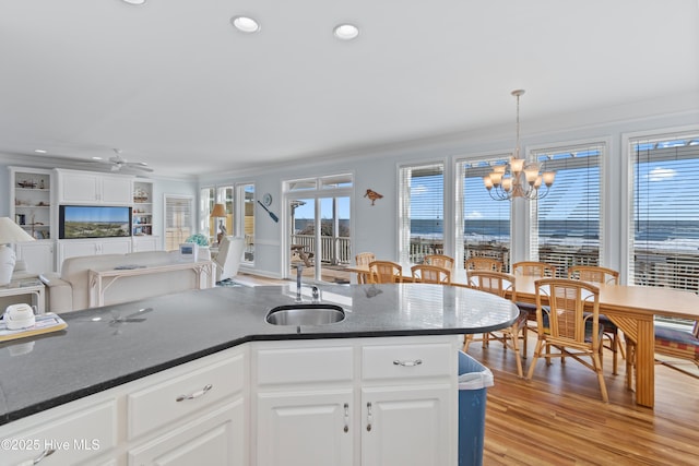 kitchen with light wood finished floors, open floor plan, ornamental molding, white cabinetry, and a sink