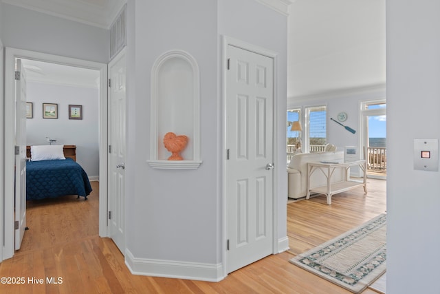 corridor featuring light wood finished floors, visible vents, baseboards, and ornamental molding