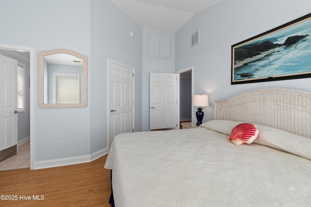 bedroom with visible vents, wood finished floors, baseboards, and high vaulted ceiling