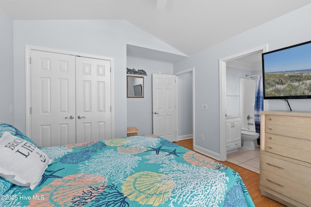 bedroom featuring baseboards, light wood finished floors, ensuite bath, vaulted ceiling, and a closet