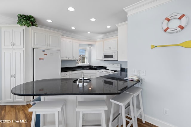 kitchen with a sink, dark countertops, white appliances, a peninsula, and crown molding