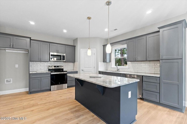 kitchen featuring light wood-type flooring, a sink, light stone counters, a center island, and appliances with stainless steel finishes