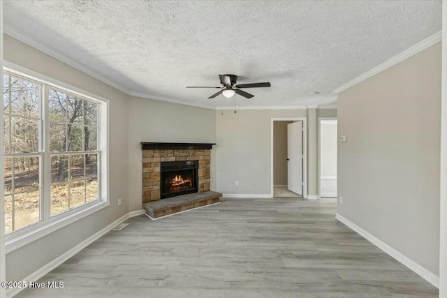 unfurnished living room featuring a ceiling fan, baseboards, light wood finished floors, a fireplace, and crown molding