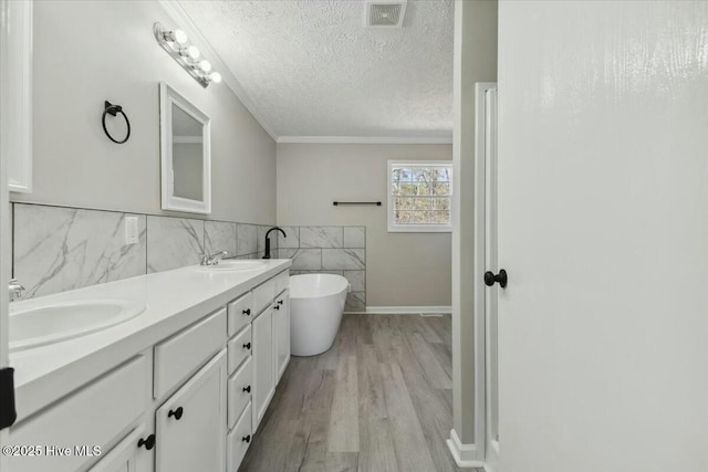 bathroom featuring wood finished floors, visible vents, a freestanding tub, a sink, and a textured ceiling