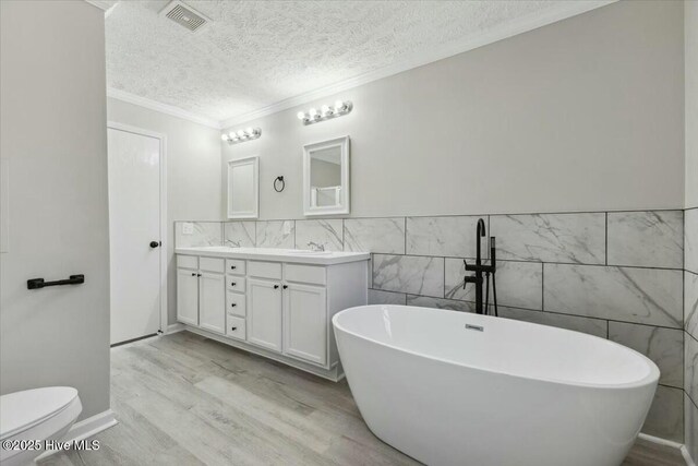 full bathroom featuring visible vents, wood finished floors, double vanity, a freestanding tub, and a textured ceiling