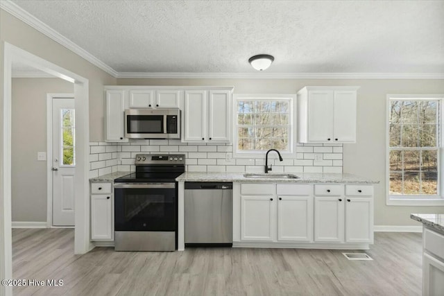 kitchen with decorative backsplash, light wood-style flooring, white cabinets, stainless steel appliances, and a sink