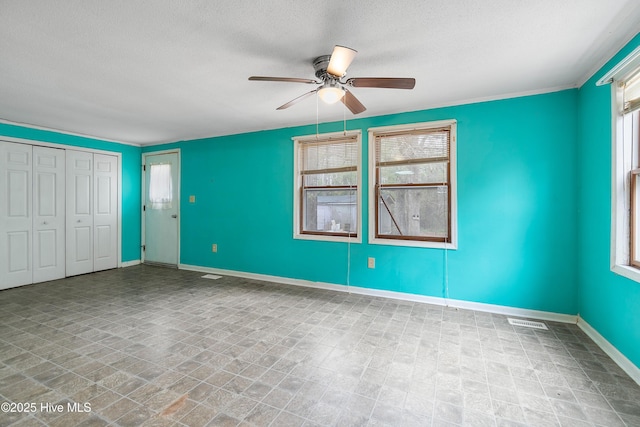 empty room with visible vents, ceiling fan, a textured ceiling, and baseboards