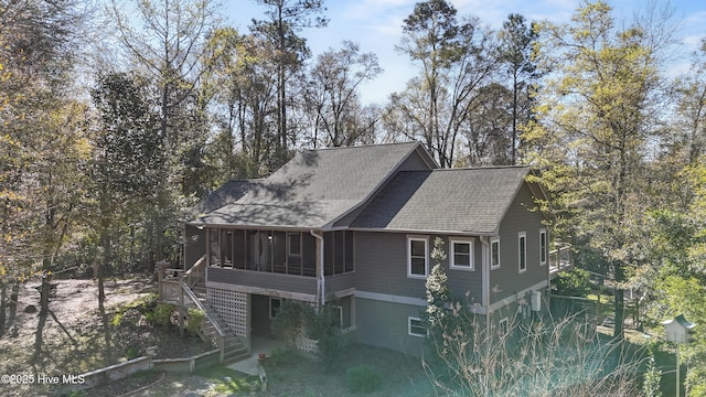 view of side of property with a sunroom, roof with shingles, stairway, and view of scattered trees